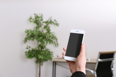 Photo of Woman holding mobile phone with blank screen in office, closeup. Space for text
