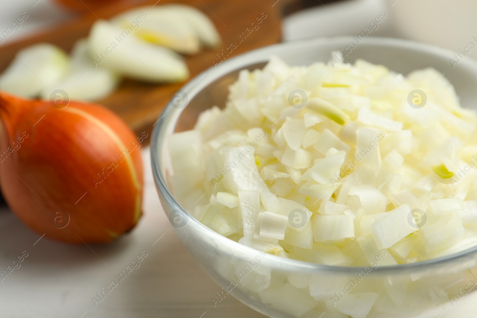 Photo of Chopped onion in bowl on white wooden table, closeup