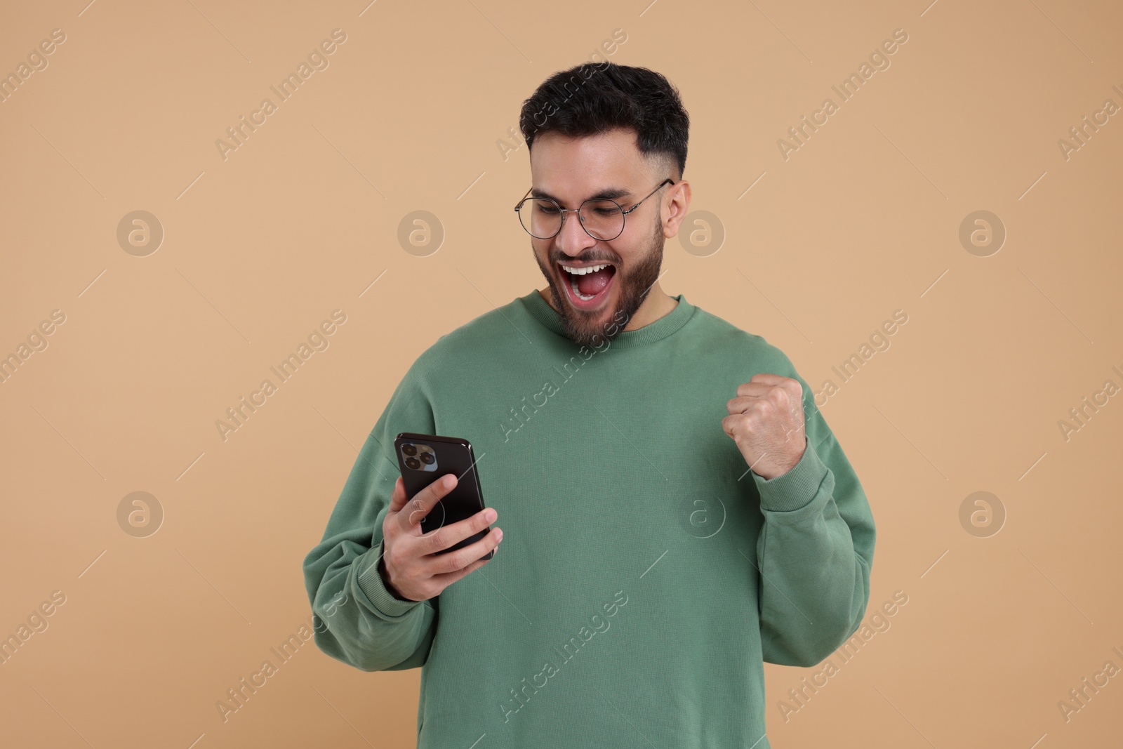 Photo of Happy young man using smartphone on beige background