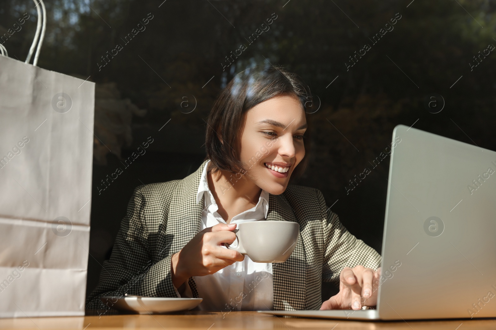Photo of Special Promotion. Happy young woman with cup of drink using laptop at table in cafe
