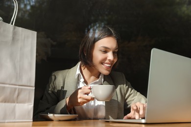 Photo of Special Promotion. Happy young woman with cup of drink using laptop at table in cafe