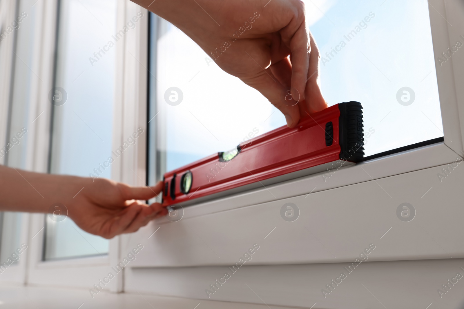 Photo of Worker using bubble level after plastic window installation indoors, closeup