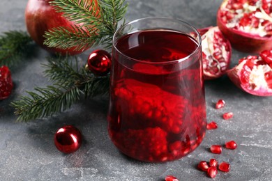 Photo of Aromatic Sangria drink in glass, Christmas decor and pomegranates on grey textured table