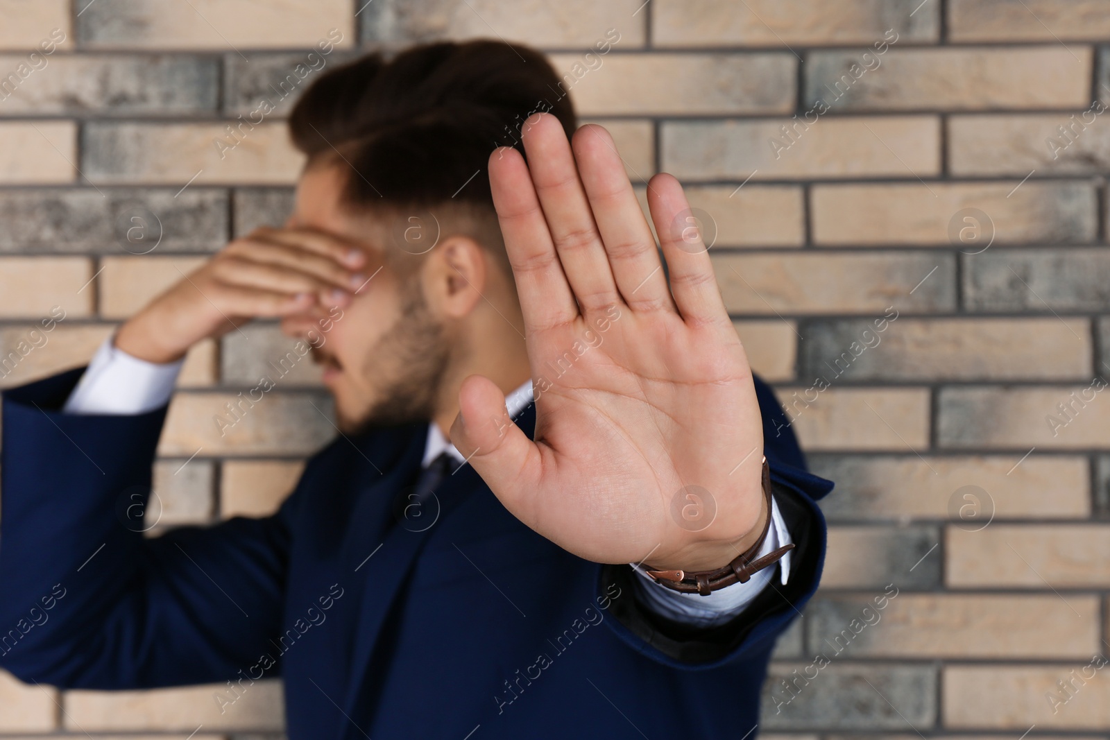 Photo of Man showing stop gesture near brick wall. Problem of sexual harassment at work