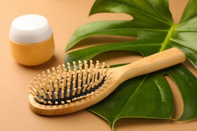 Photo of Wooden hairbrush, jar of cosmetic product and green leaf on light brown background closeup
