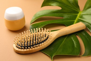 Wooden hairbrush, jar of cosmetic product and green leaf on light brown background closeup