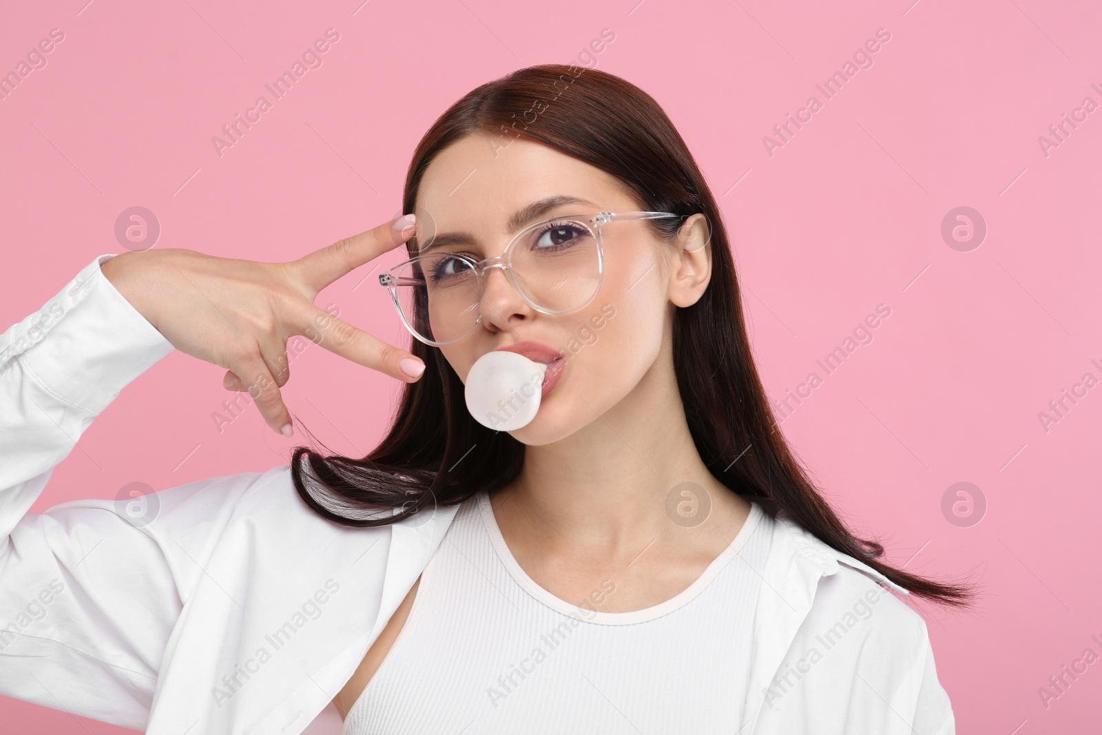 Photo of Beautiful woman in glasses blowing bubble gum and gesturing on pink background