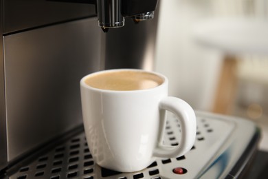 Photo of Espresso machine with cup of fresh coffee on drip tray against blurred background, closeup
