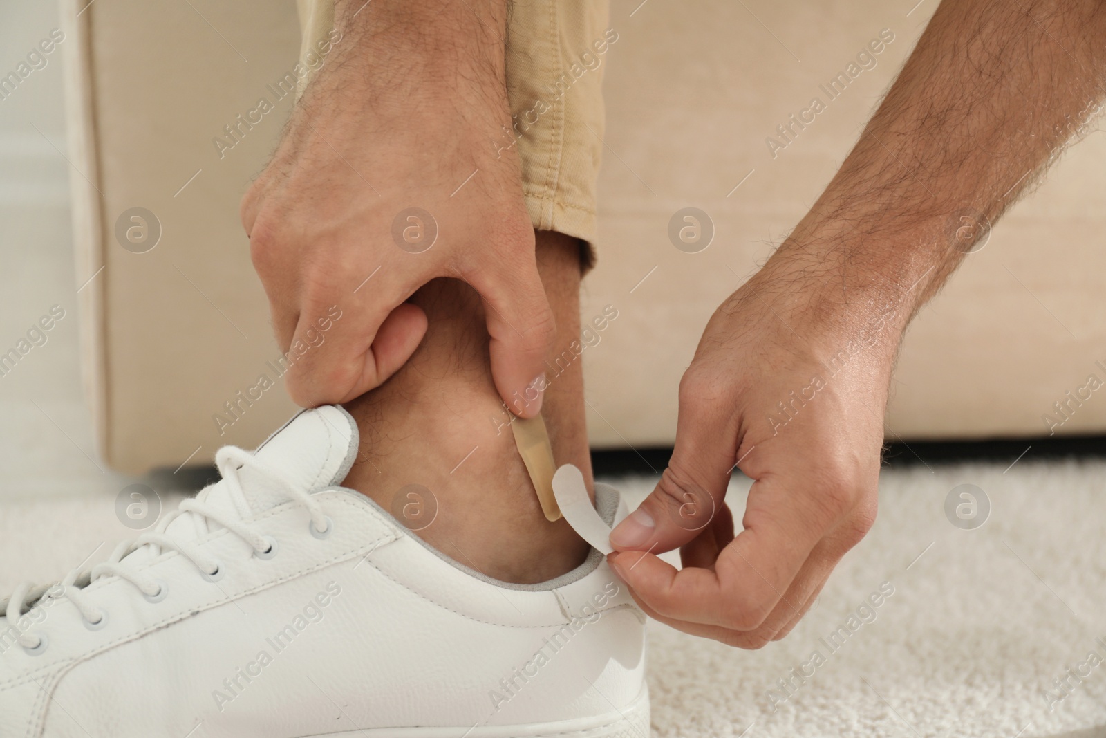 Photo of Man putting sticking plaster onto ankle indoors, closeup