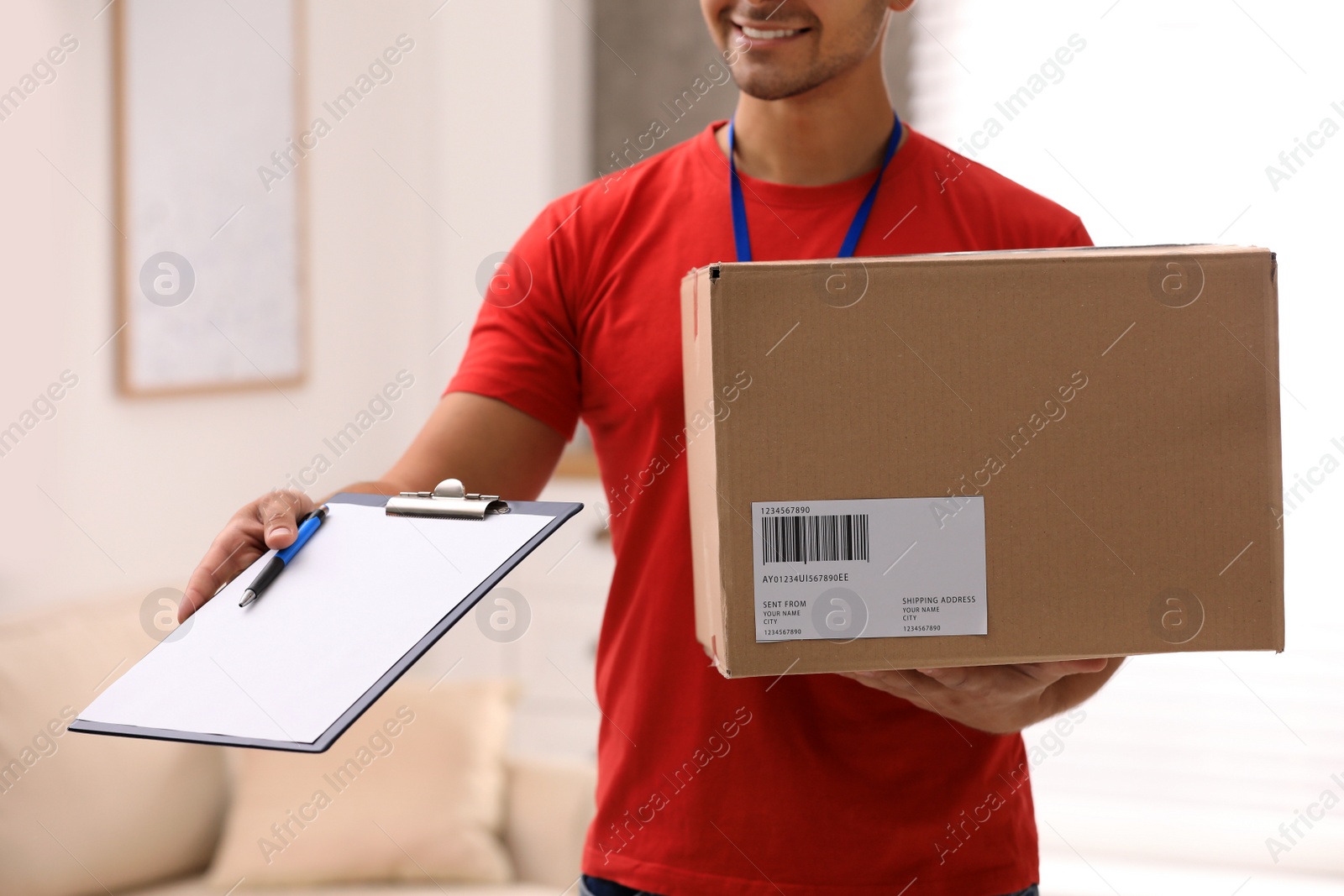 Photo of Young courier holding parcel and clipboard indoors, closeup. Delivery service