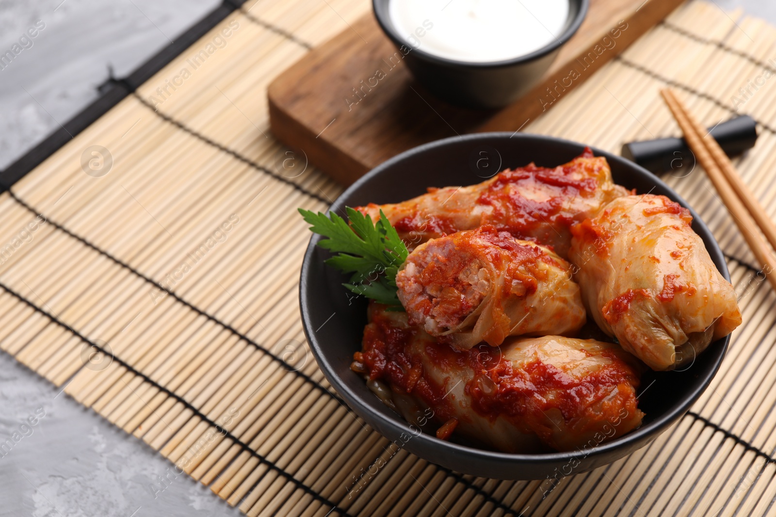 Photo of Delicious stuffed cabbage rolls cooked with tomato sauce on grey table, closeup. Space for text