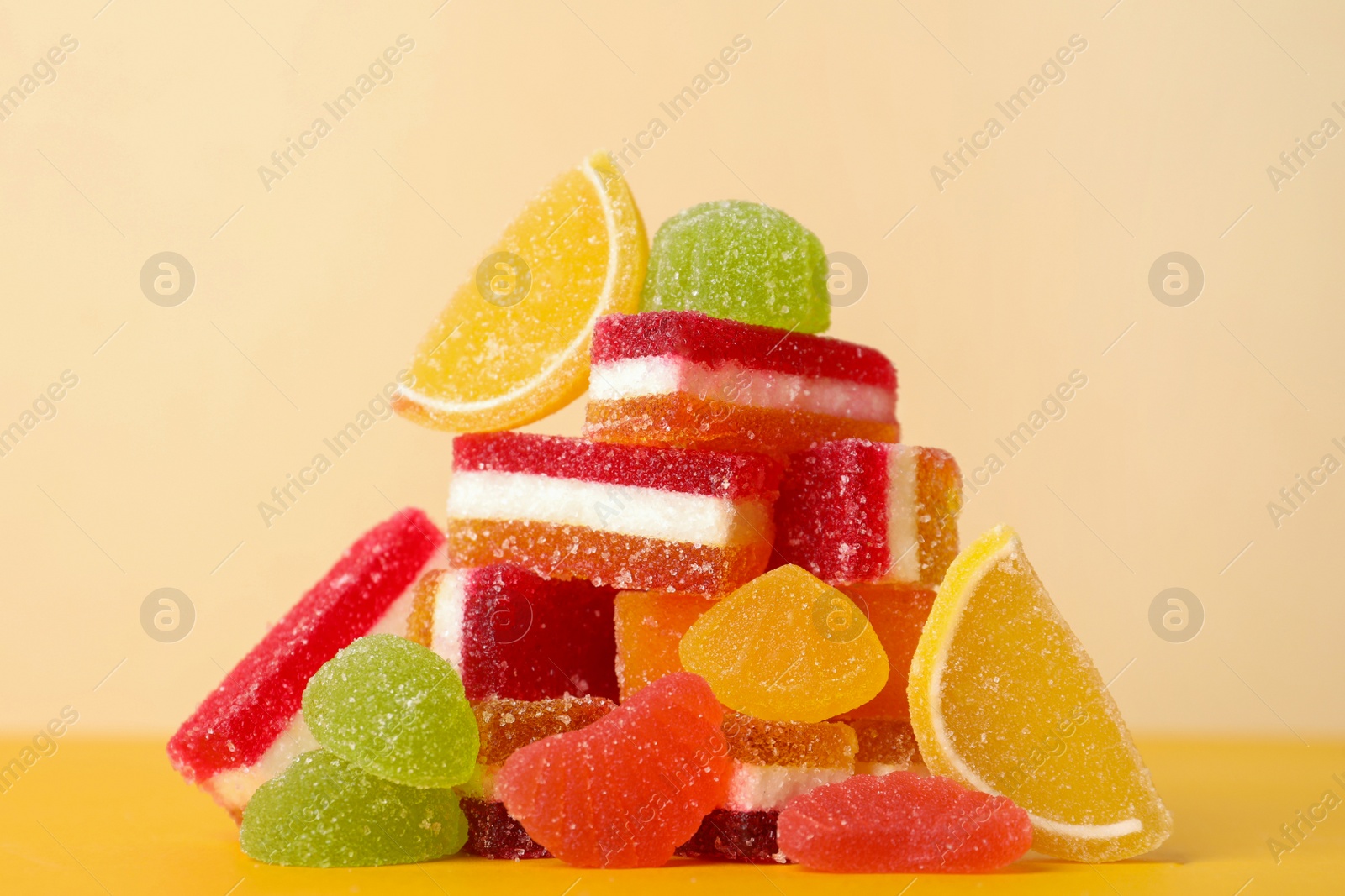 Photo of Pile of delicious bright jelly candies on yellow table