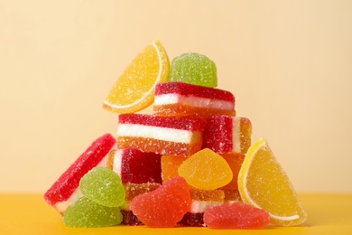 Photo of Pile of delicious bright jelly candies on yellow table