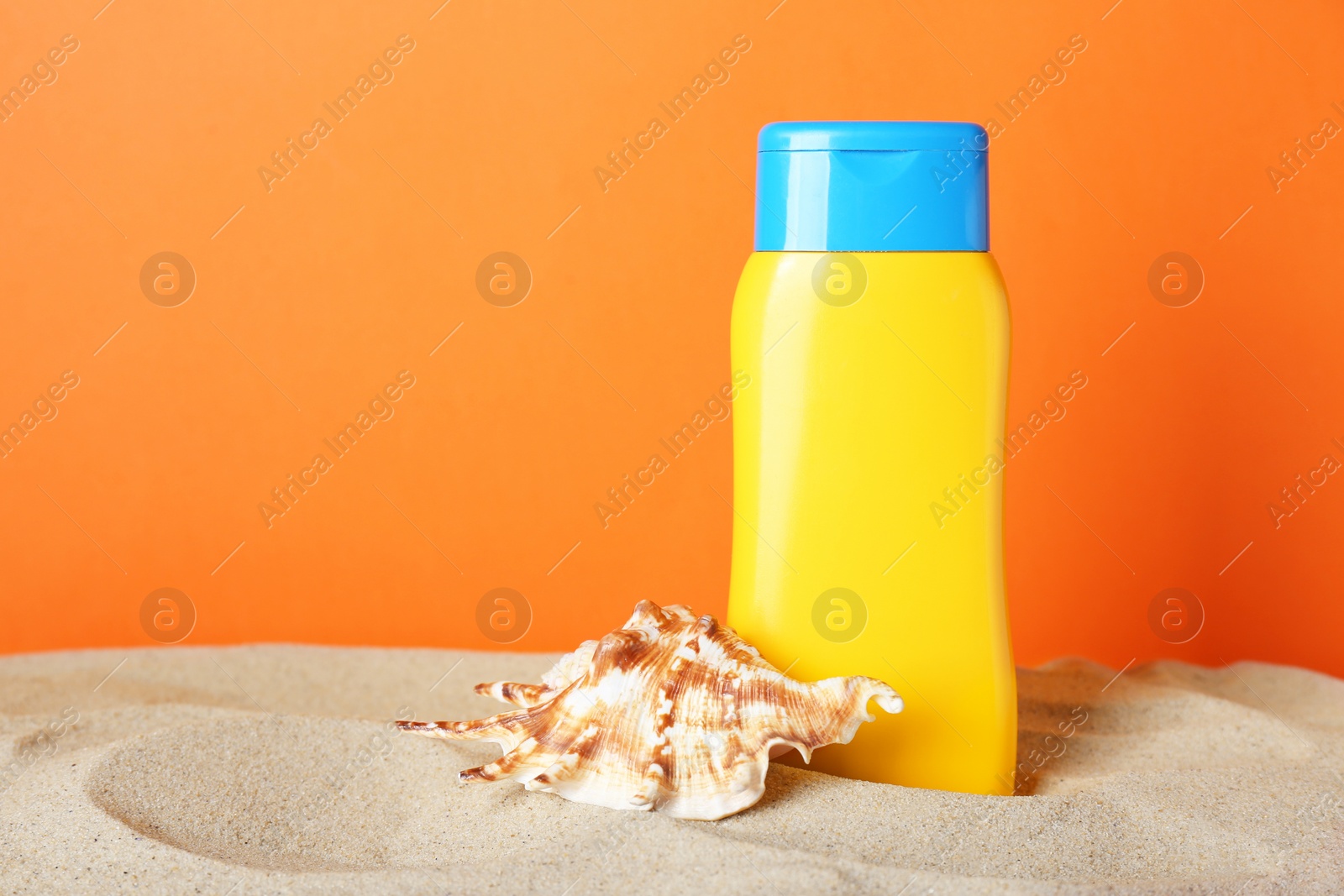 Photo of Suntan product and starfish on sand against orange background. Space for text