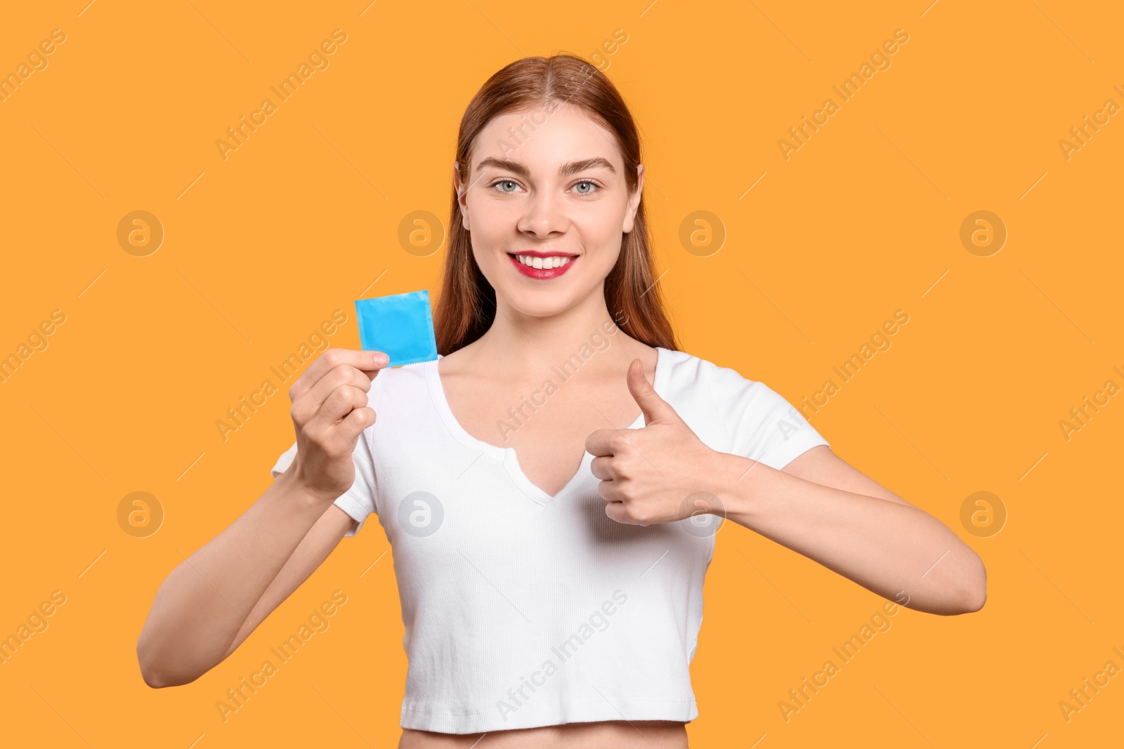 Photo of Woman holding with condom showing thumb up on yellow background. Safe sex