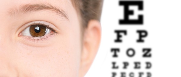 Closeup view of child and blurred eye chart on background, banner design. Visiting ophthalmologist 
