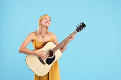 Happy hippie woman playing guitar on light blue background