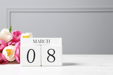 International Women's day - 8th of March. Wooden block calendar and beautiful flowers on white table, space for text