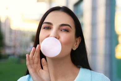 Photo of Beautiful woman blowing gum near building outdoors