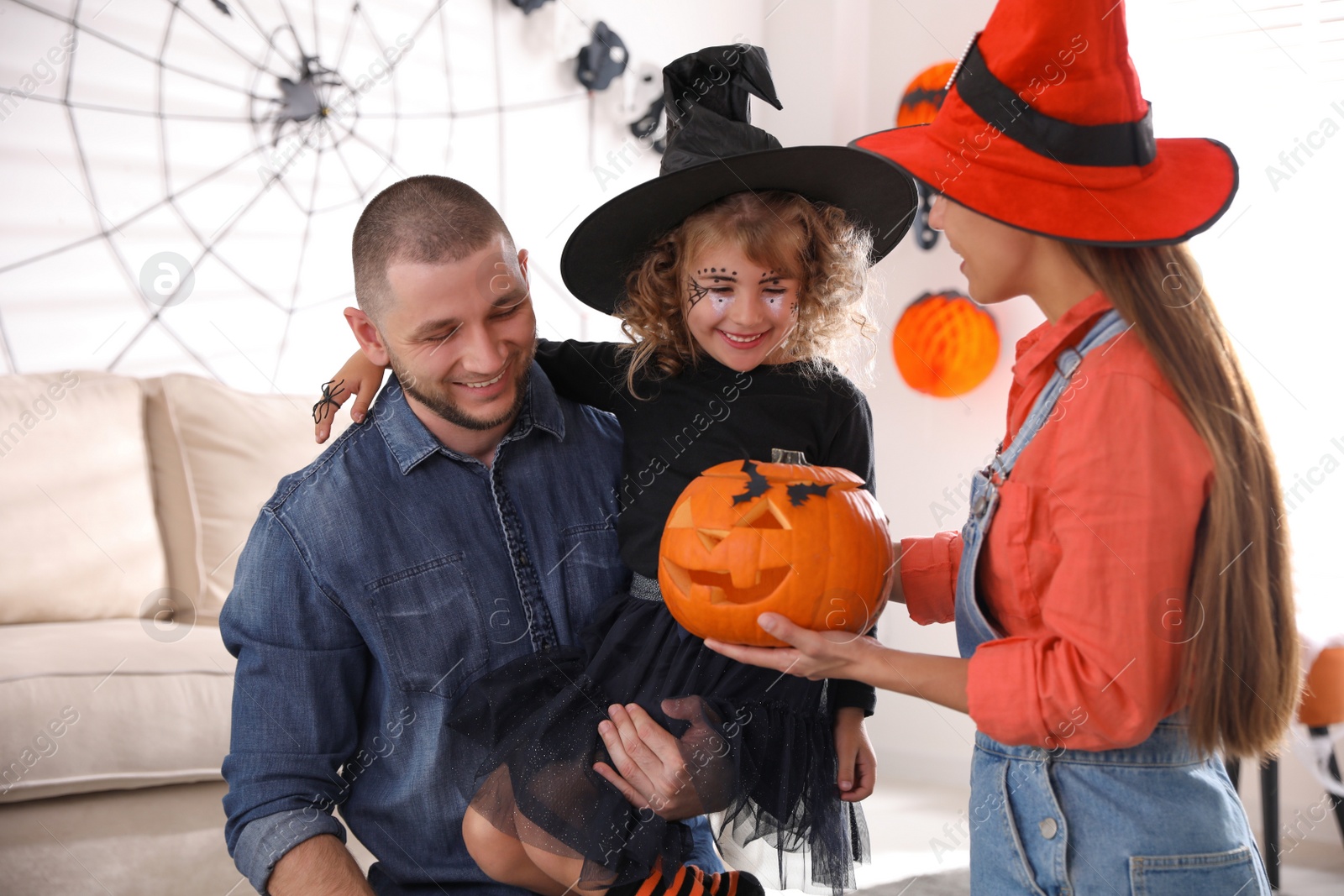 Photo of Parents and cute little girl with pumpkin having Halloween party at home