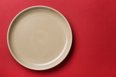 Empty beige ceramic plate on red background, top view. Space for text
