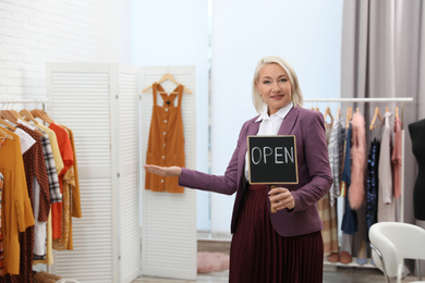 Photo of Female business owner holding OPEN sign in boutique