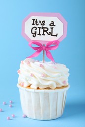 Beautifully decorated baby shower cupcake for girl with cream and topper on light blue background