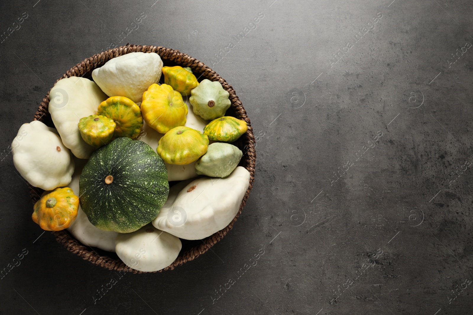 Photo of Fresh ripe pattypan squashes in wicker bowl on grey table, top view. Space for text