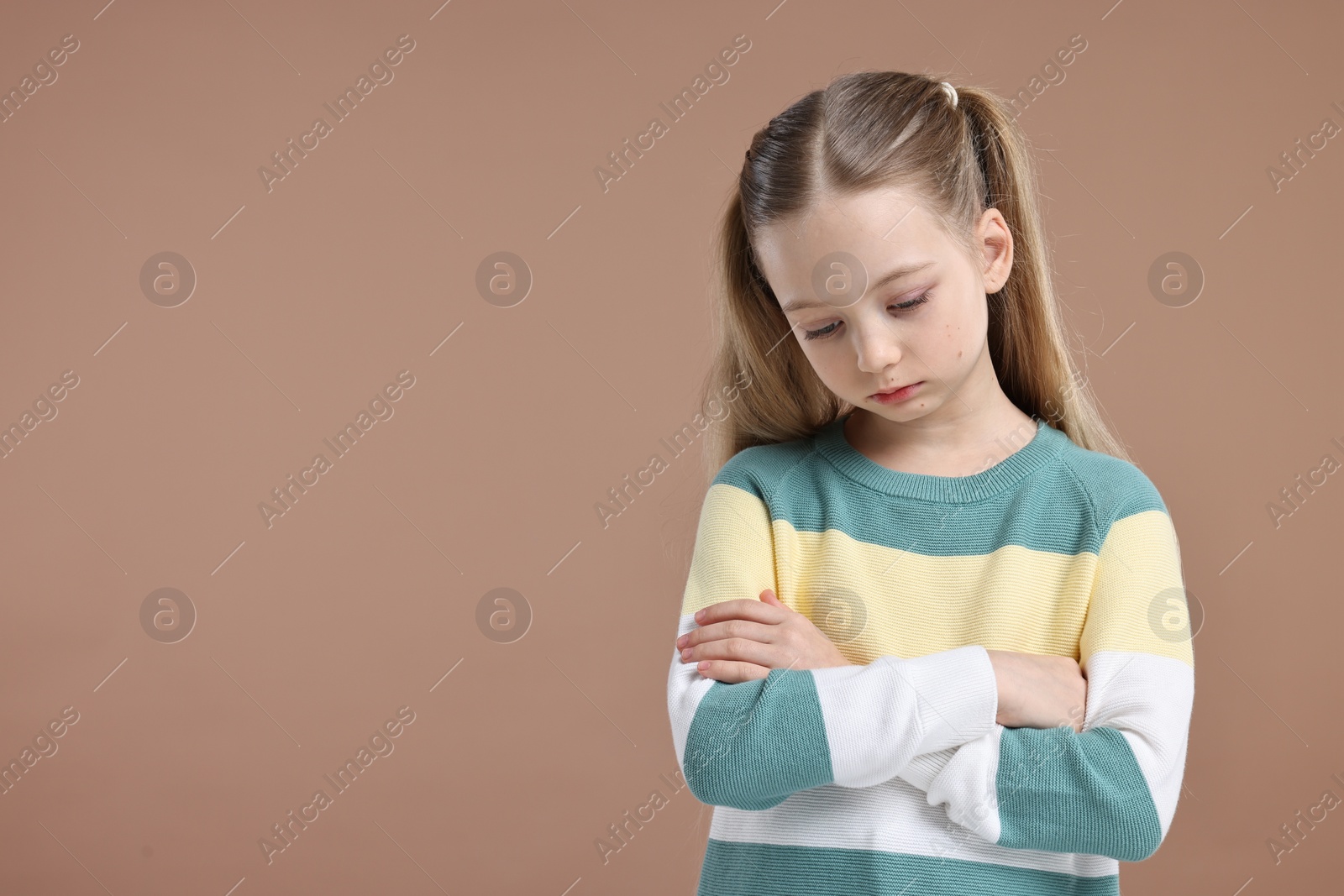 Photo of Portrait of sad girl with crossed arms on light brown background, space for text