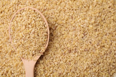 Photo of Wooden spoon and raw bulgur as background, top view. Space for text
