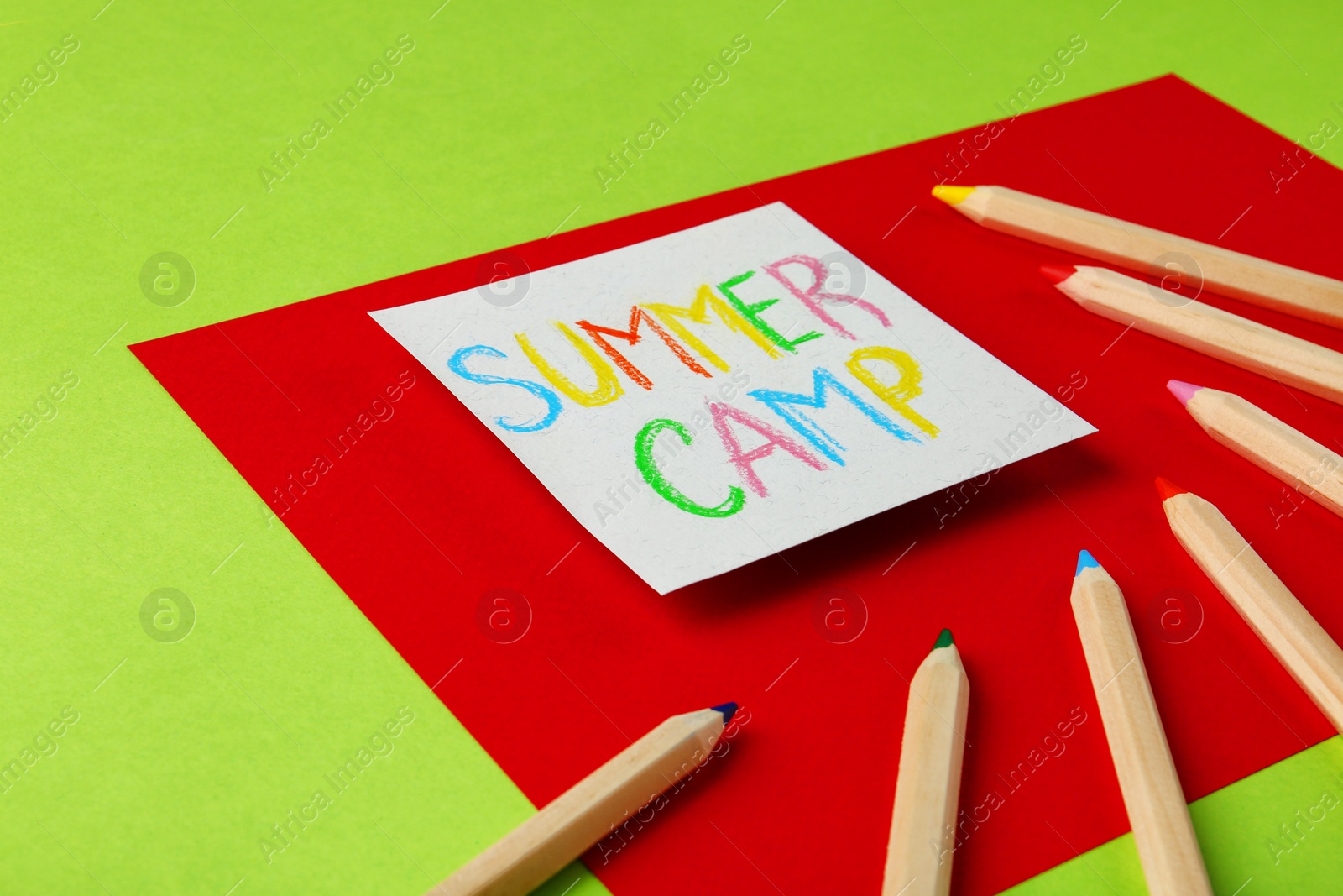 Photo of Paper with written text SUMMER CAMP and different pencils on color background