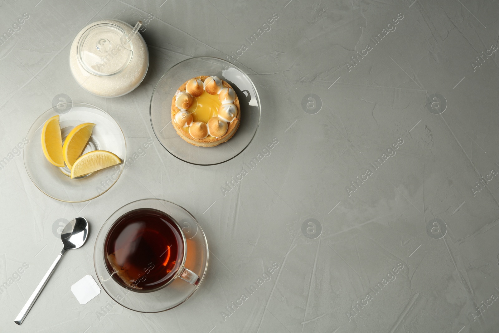 Photo of Flat lay composition with tea bag in ceramic cup of hot water and dessert on grey table. Space for text