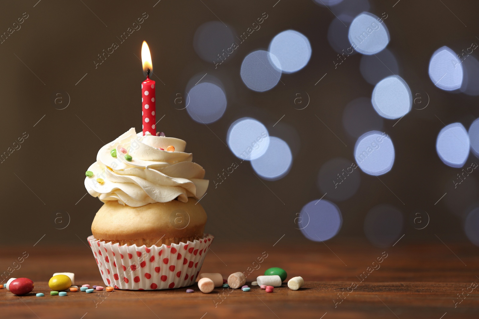 Photo of Birthday cupcake with candle on wooden table against blurred lights. Space for text