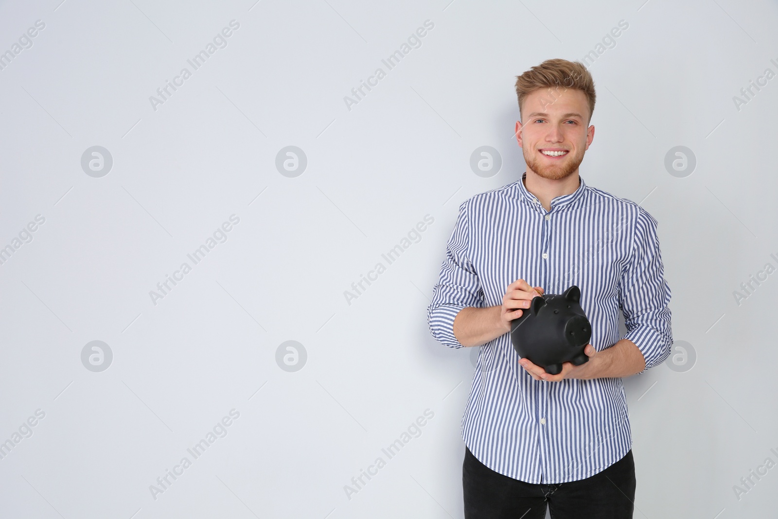 Photo of Young man putting coin into piggy bank on light background. Space for text