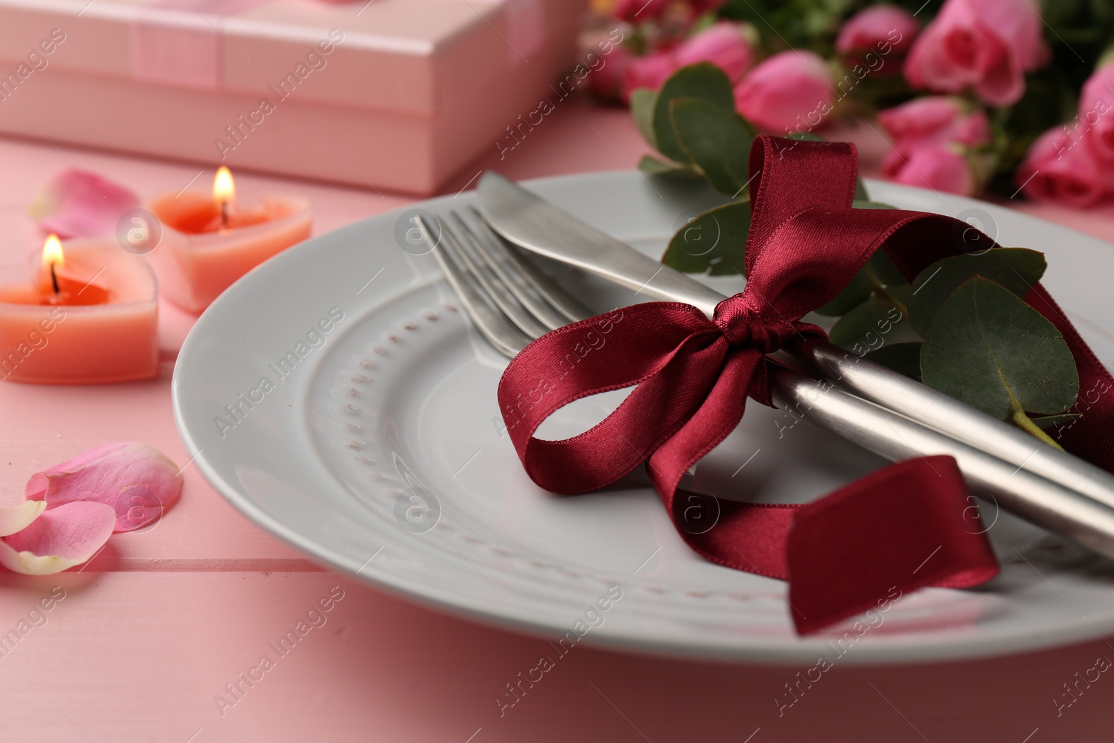 Photo of Place setting with roses and candles on pink wooden table, closeup. Romantic dinner