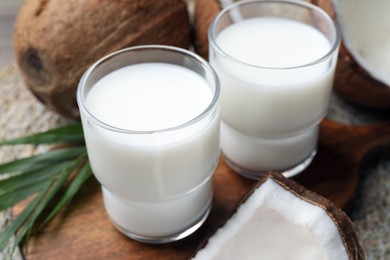 Glasses of delicious coconut milk, palm leaf and coconuts on table