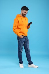 Happy young man using smartphone on light blue background