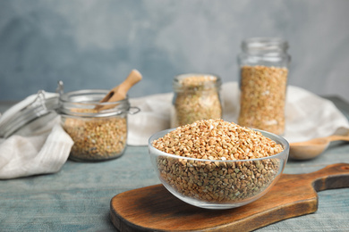 Uncooked green buckwheat grains in bowl on light blue wooden table