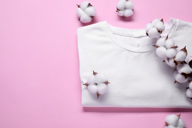 Photo of Cotton branch with fluffy flowers and white t-shirt on pink background, flat lay. Space for text