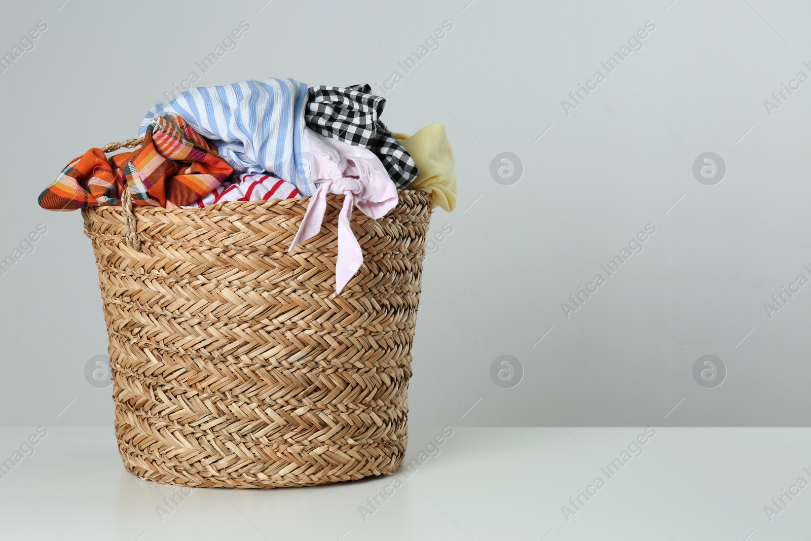 Photo of Wicker laundry basket with different clothes on light background. Space for text