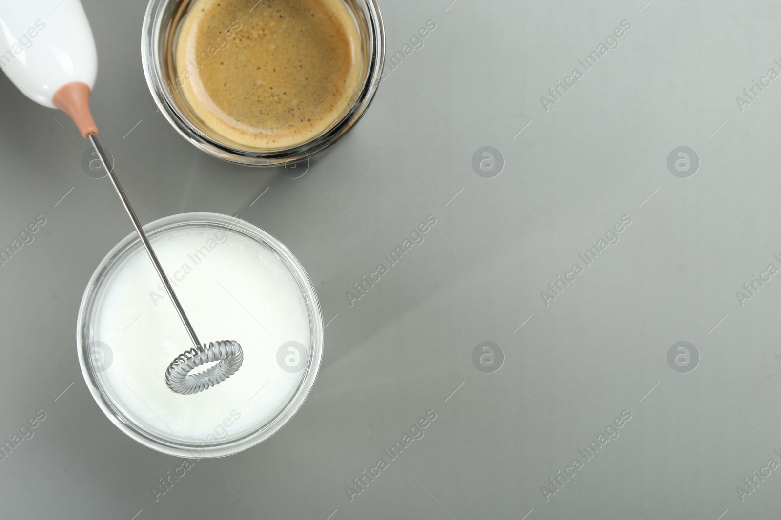 Photo of Mini mixer (milk frother), whipped milk and coffee in glasses on grey background, flat lay. Space for text