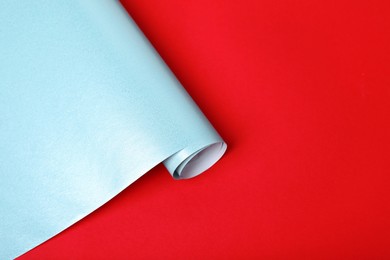 Photo of Roll of light blue wrapping paper on red background, closeup. Space for text