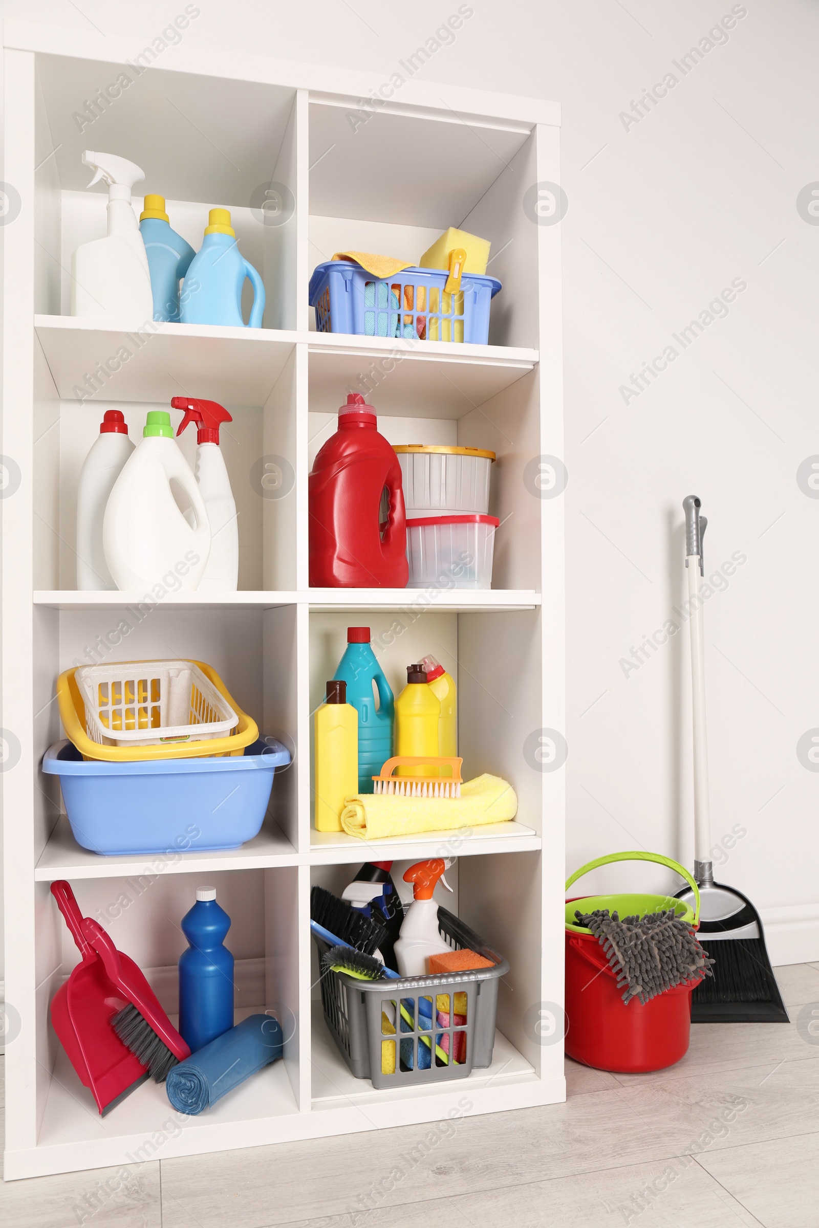 Photo of Shelving unit with detergents and cleaning tools near white wall indoors