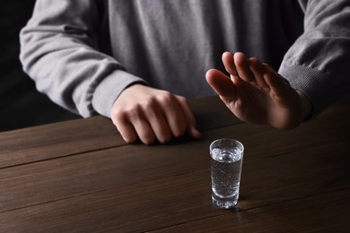 Photo of Man refusing to drink vodka at wooden table, closeup. Alcohol addiction