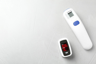 Photo of Modern fingertip pulse oximeter and non contact infrared thermometer on light grey stone background, flat lay. Space for text