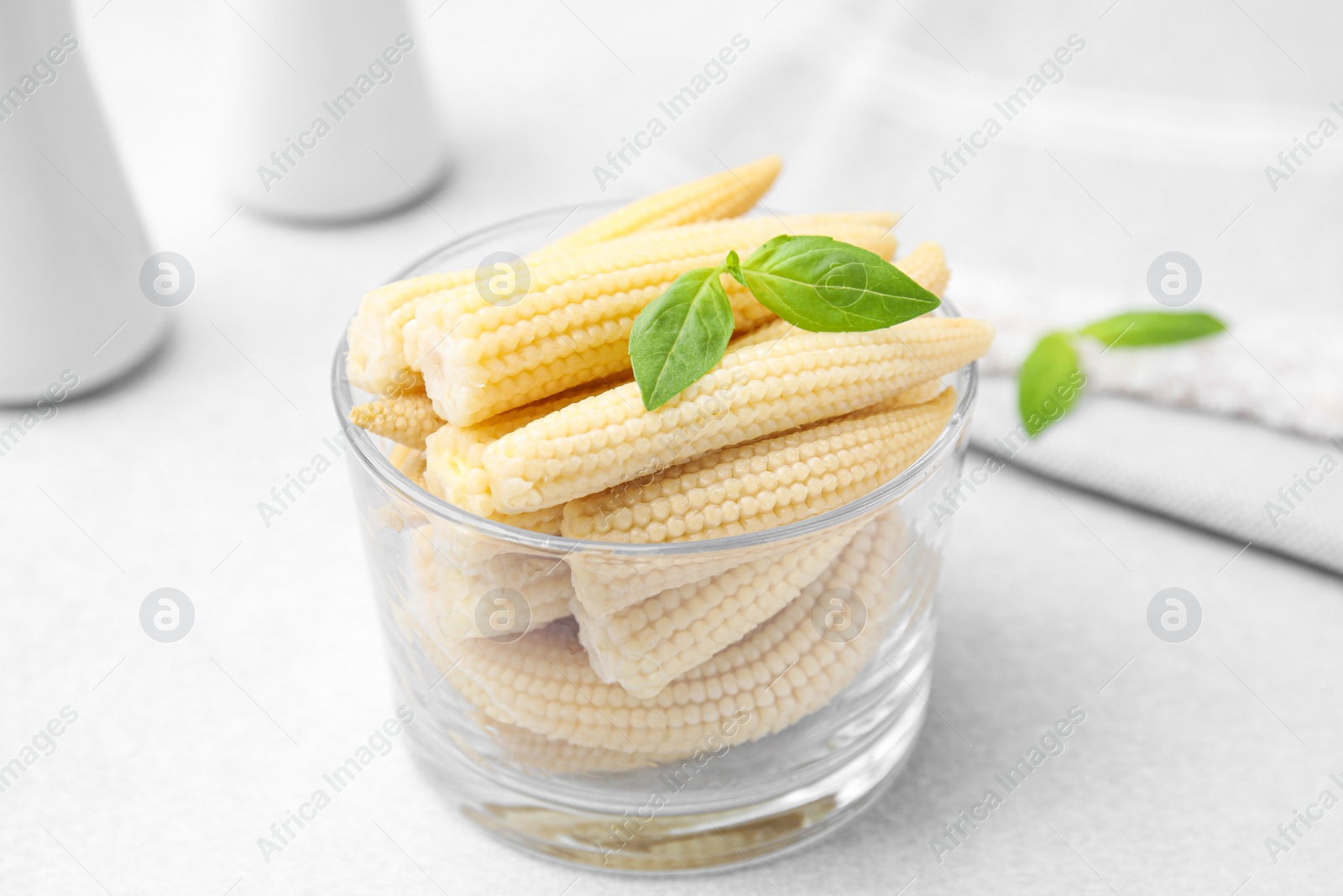 Photo of Canned baby corns with basil on white table, closeup