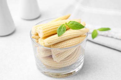 Canned baby corns with basil on white table, closeup