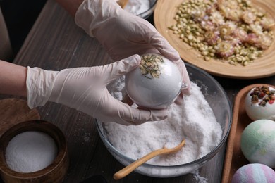 Photo of Woman in gloves making bath bomb at wooden table, closeup