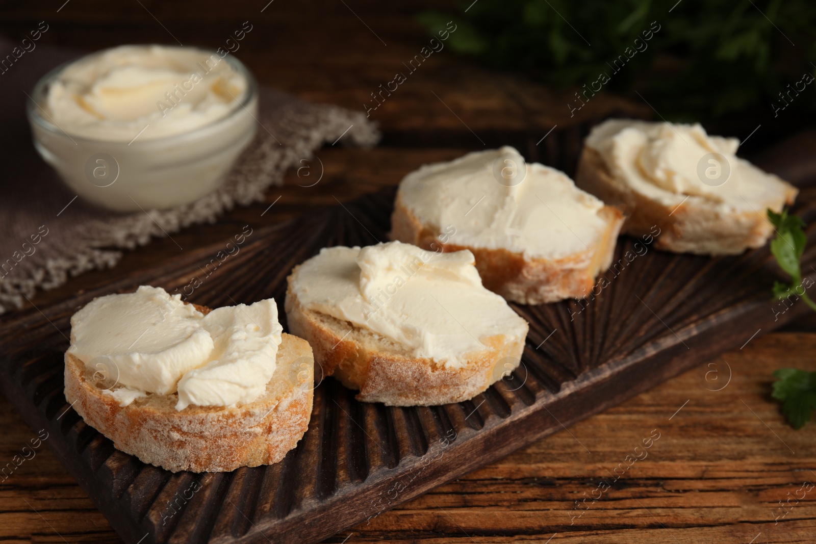 Photo of Bread with cream cheese on wooden board, closeup