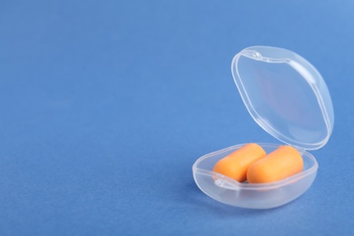 Photo of Pair of orange ear plugs in case on blue background. Space for text